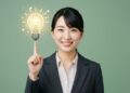 笑顔のビジネスウーマンが電球のアイコンを指さし、ひらめきを表現している画像