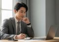 スーツ姿のビジネスパーソンがデスクでノートにメモを取りながら起業計画を立てている様子