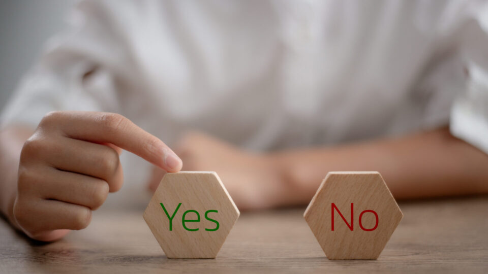 机の上で「Yes」と「No」と書かれた木製ブロックを指で選ぼうとしている様子の画像